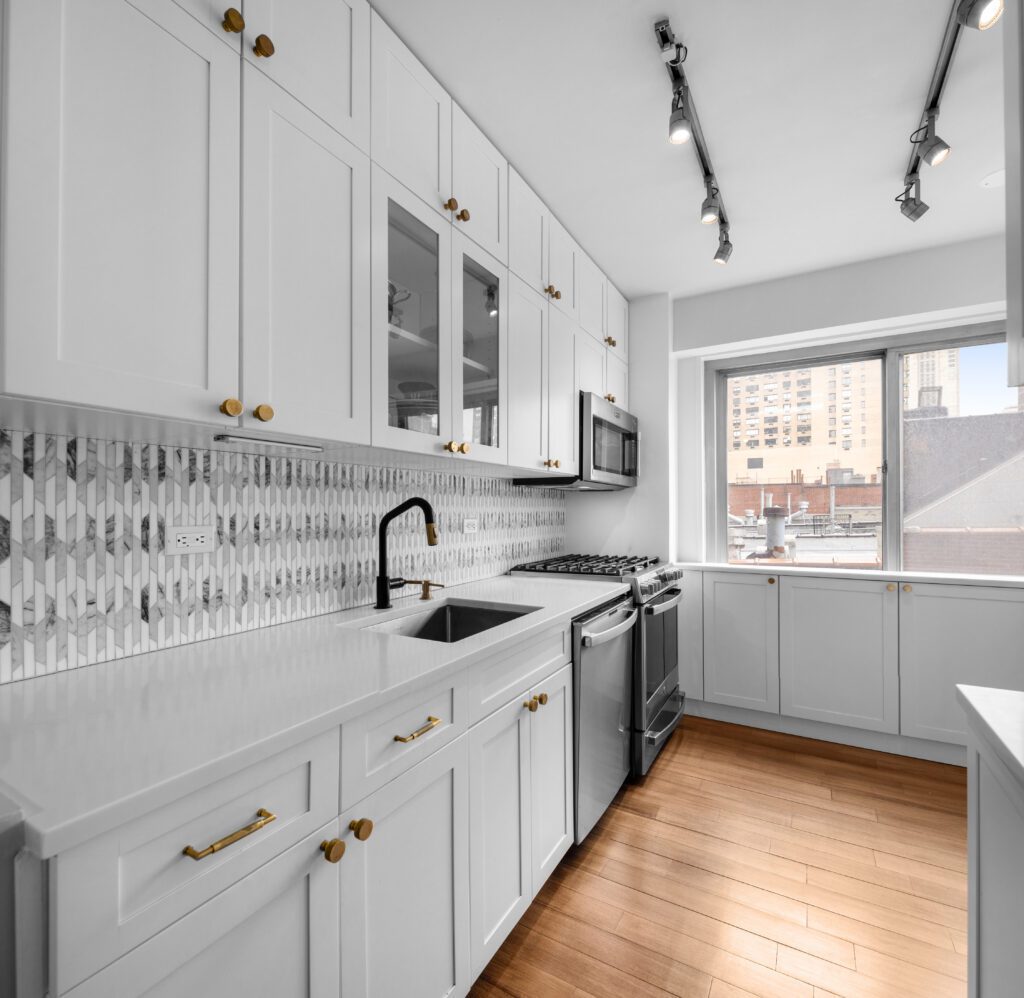 Modern kitchen renovation with white shaker cabinets, gold hardware, a stainless-steel refrigerator, and a geometric tile backsplash.